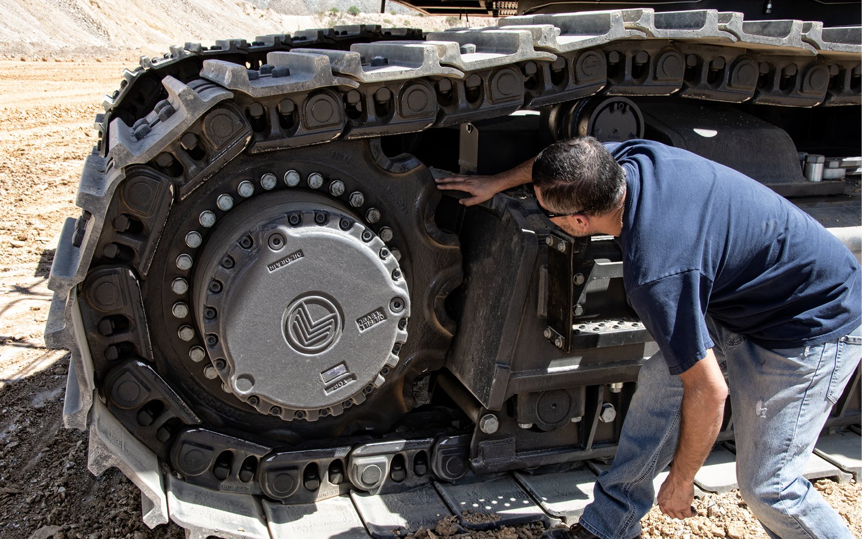 An operator inspecting the undercarriage of a large crawler excavator.