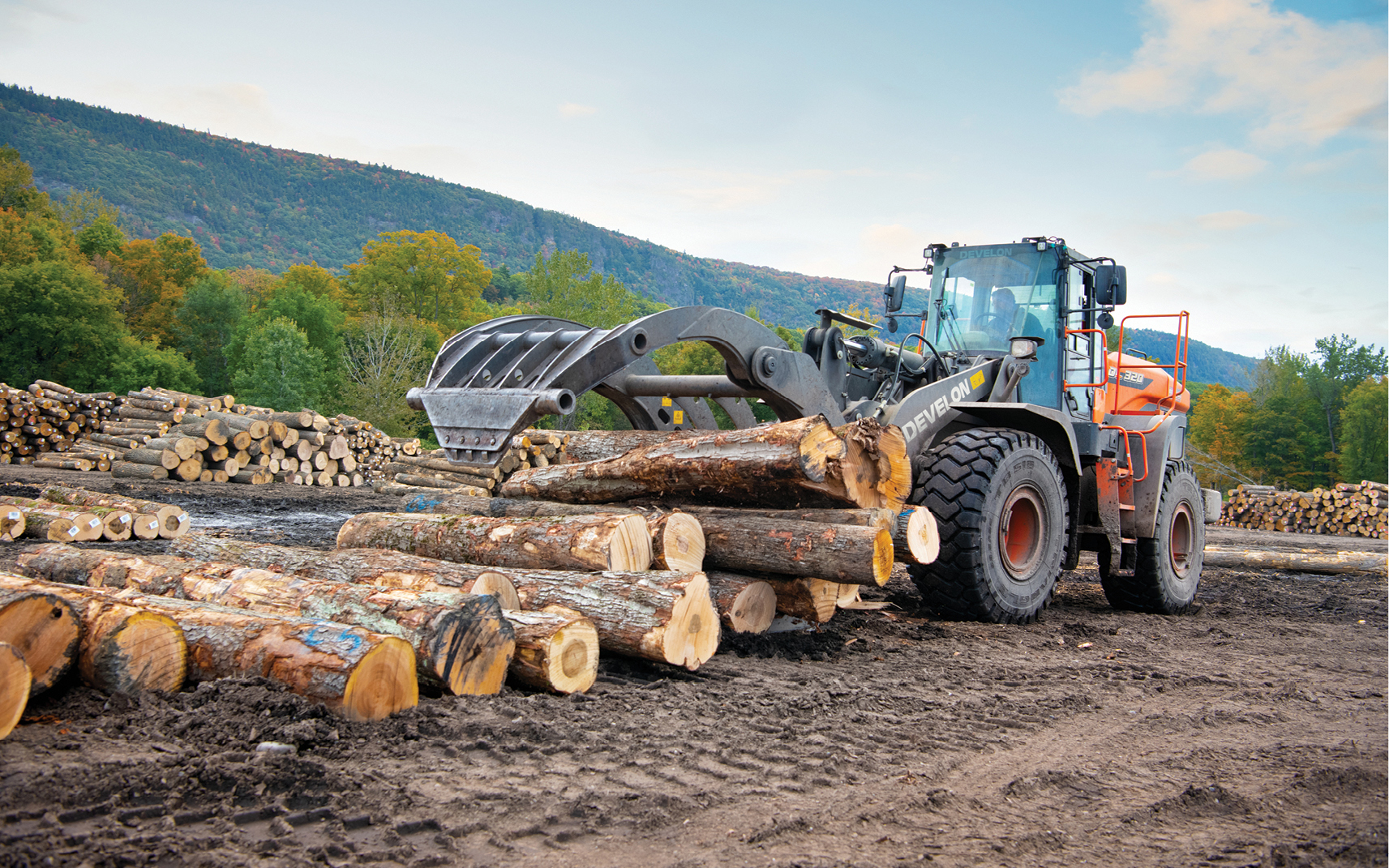 A DEVELON wheel loader equipped with a grapple attachment lifts a stack of logs.