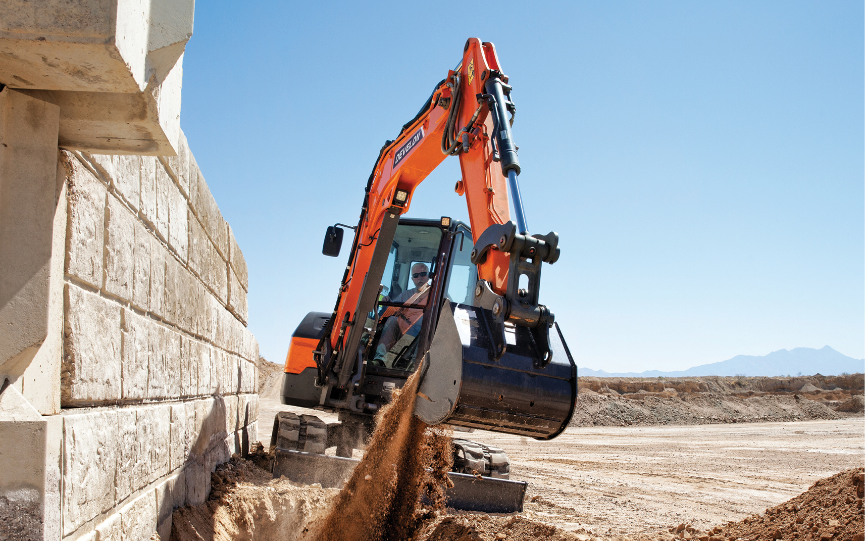 A mini excavator works next to a wall on a job site.