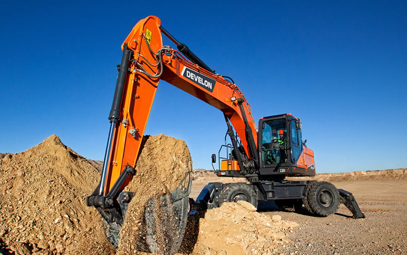 A clean DEVELON DX210W-7 wheel excavator scoops a bucket of dirt at a job site.