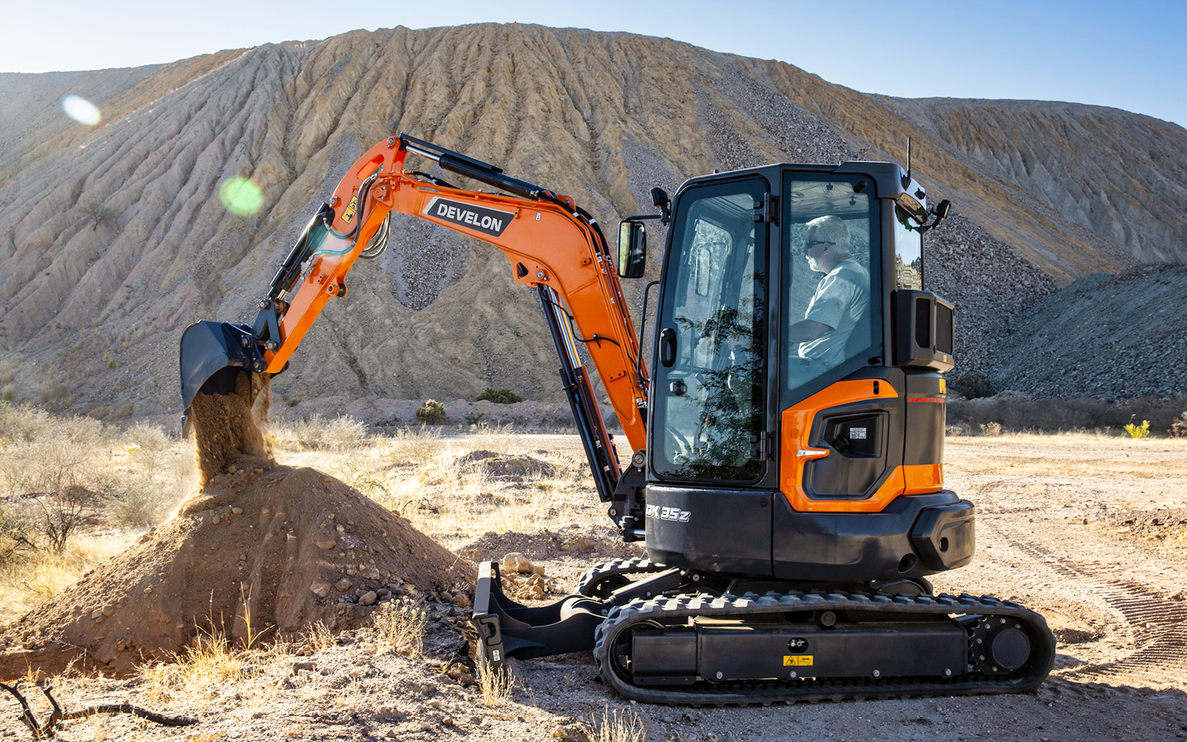 A DEVELON compact excavator empties dirt from a bucket.