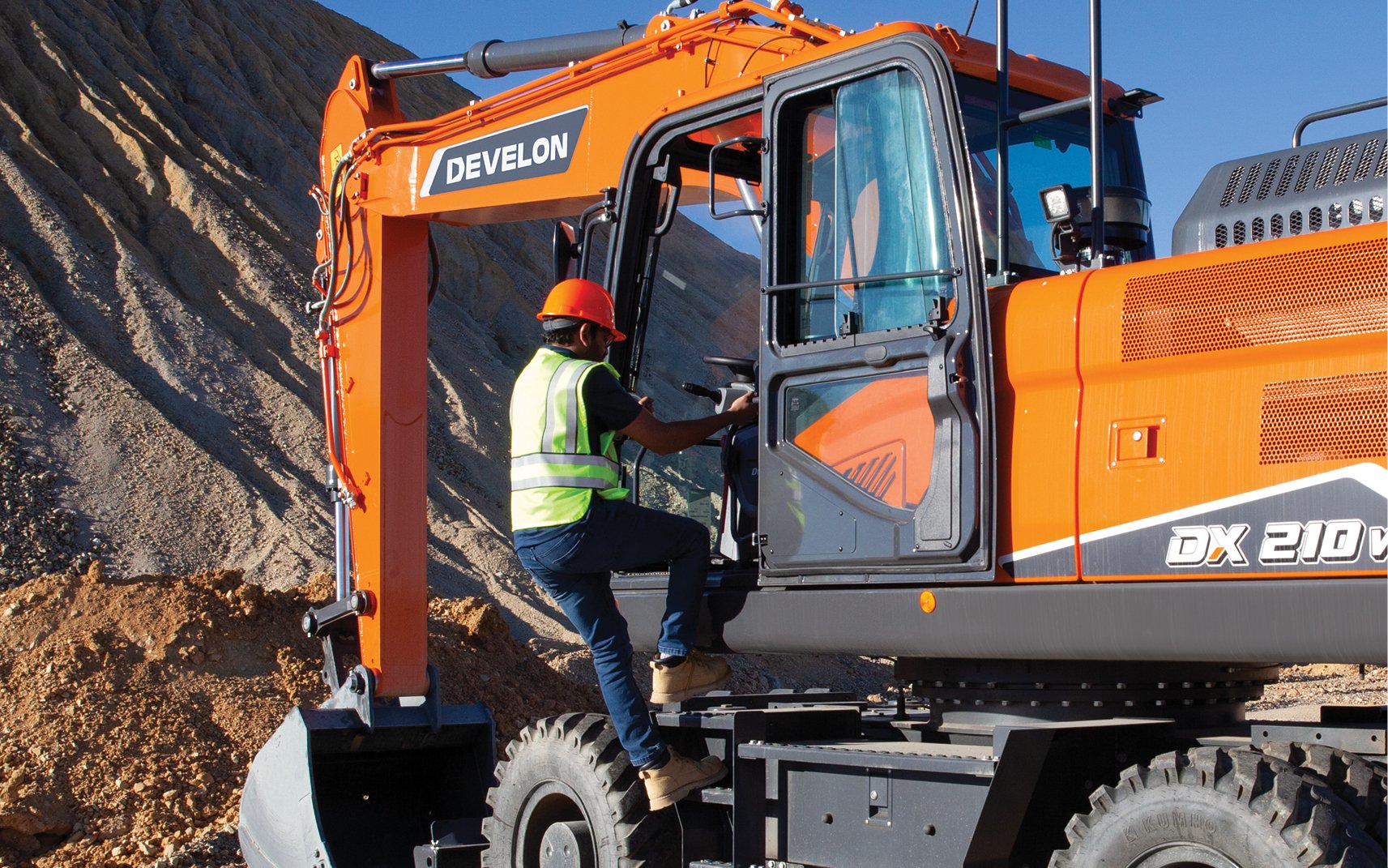 A construction worker uses three points of contact to enter the cab of a wheel excavator.