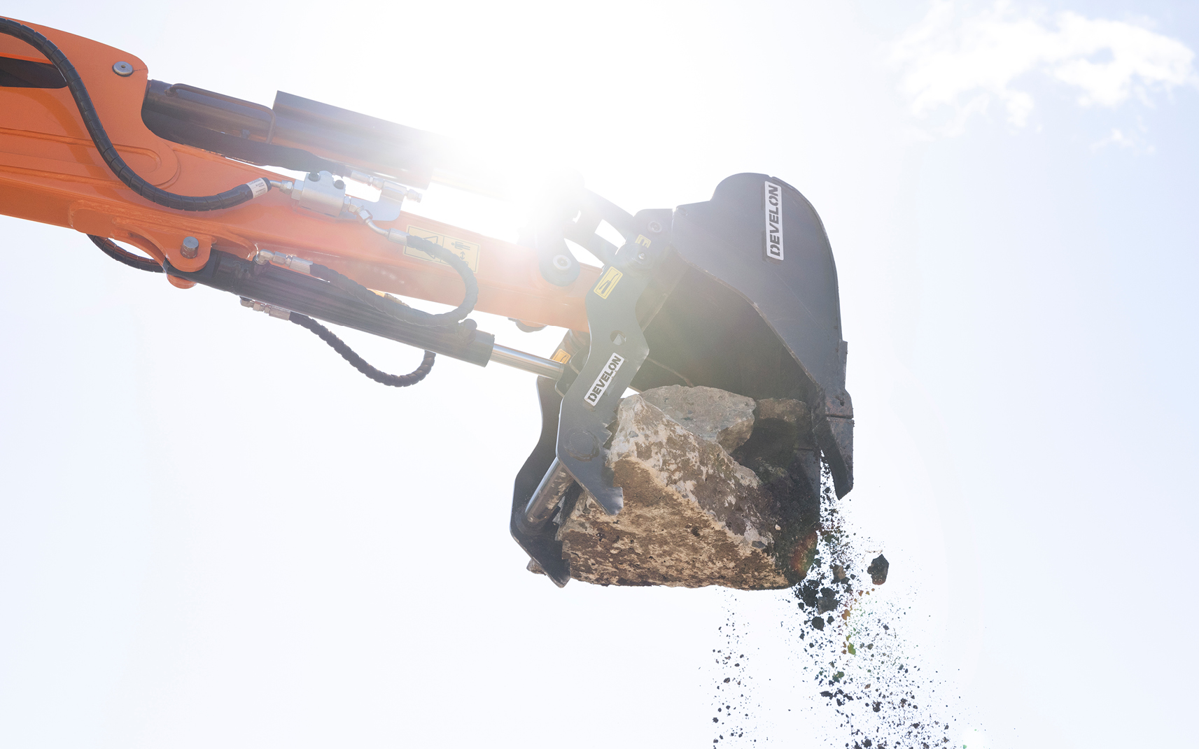 A mini excavator bucket and thumb attachment lift a rock.