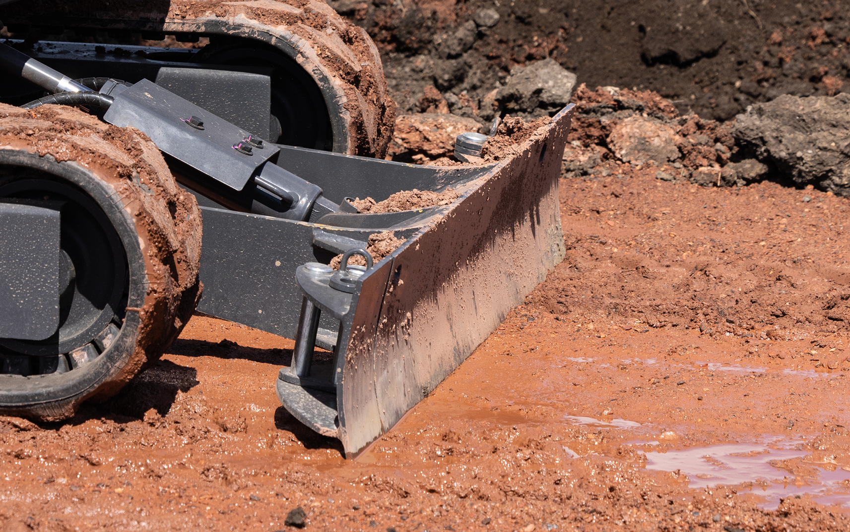 A mini excavator dozer blade grades dirt on a job site.