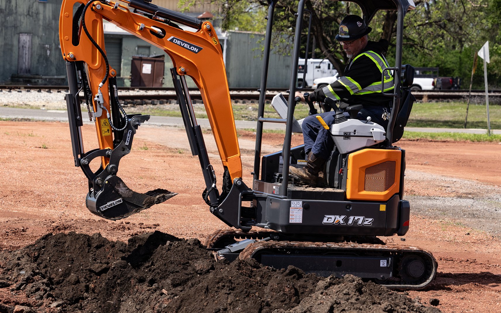 An operator backfills a trench with a mini excavator dozer blade.