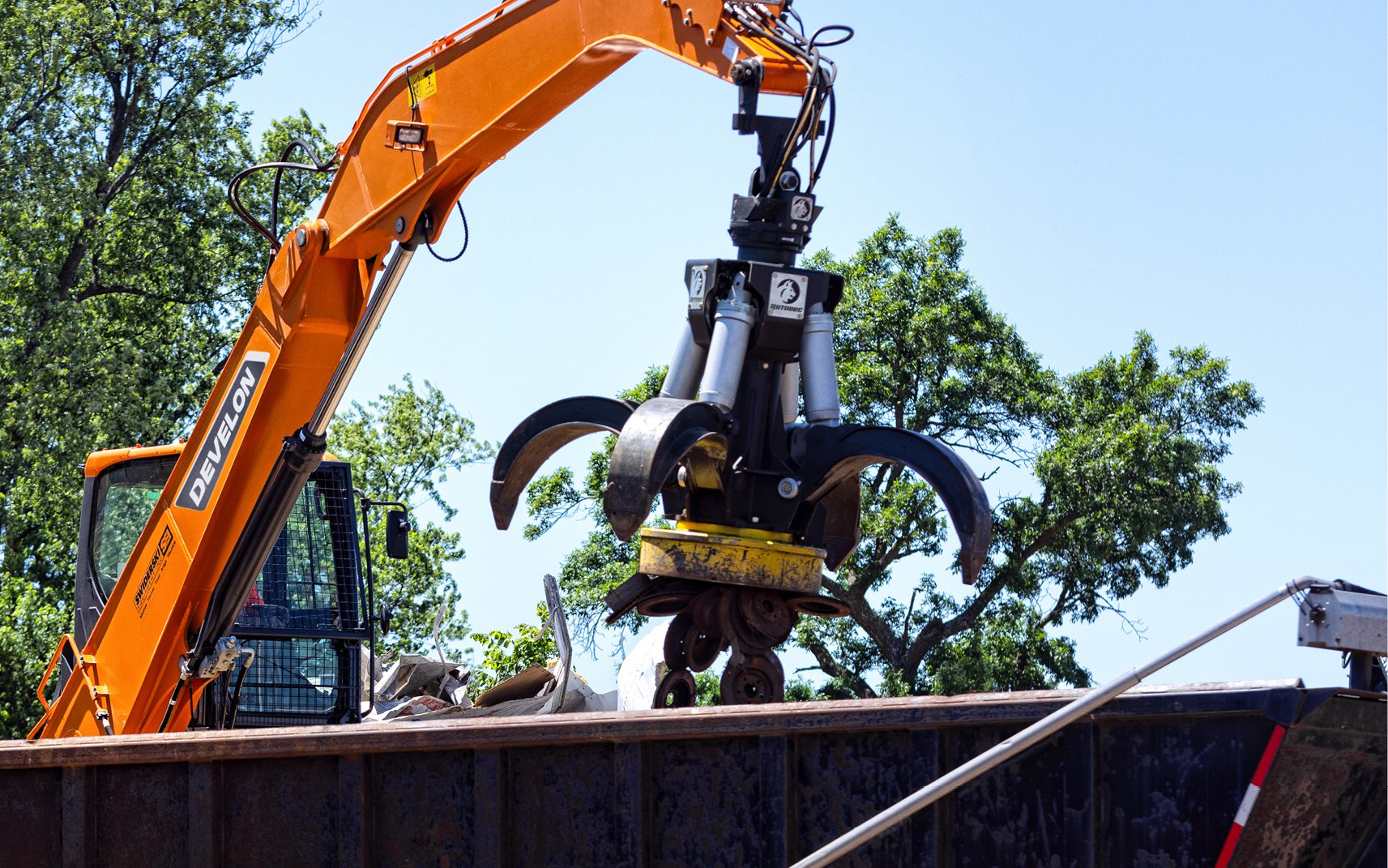 A material handler operator uses a magnet attachment to lift metal and place it in a trailer.