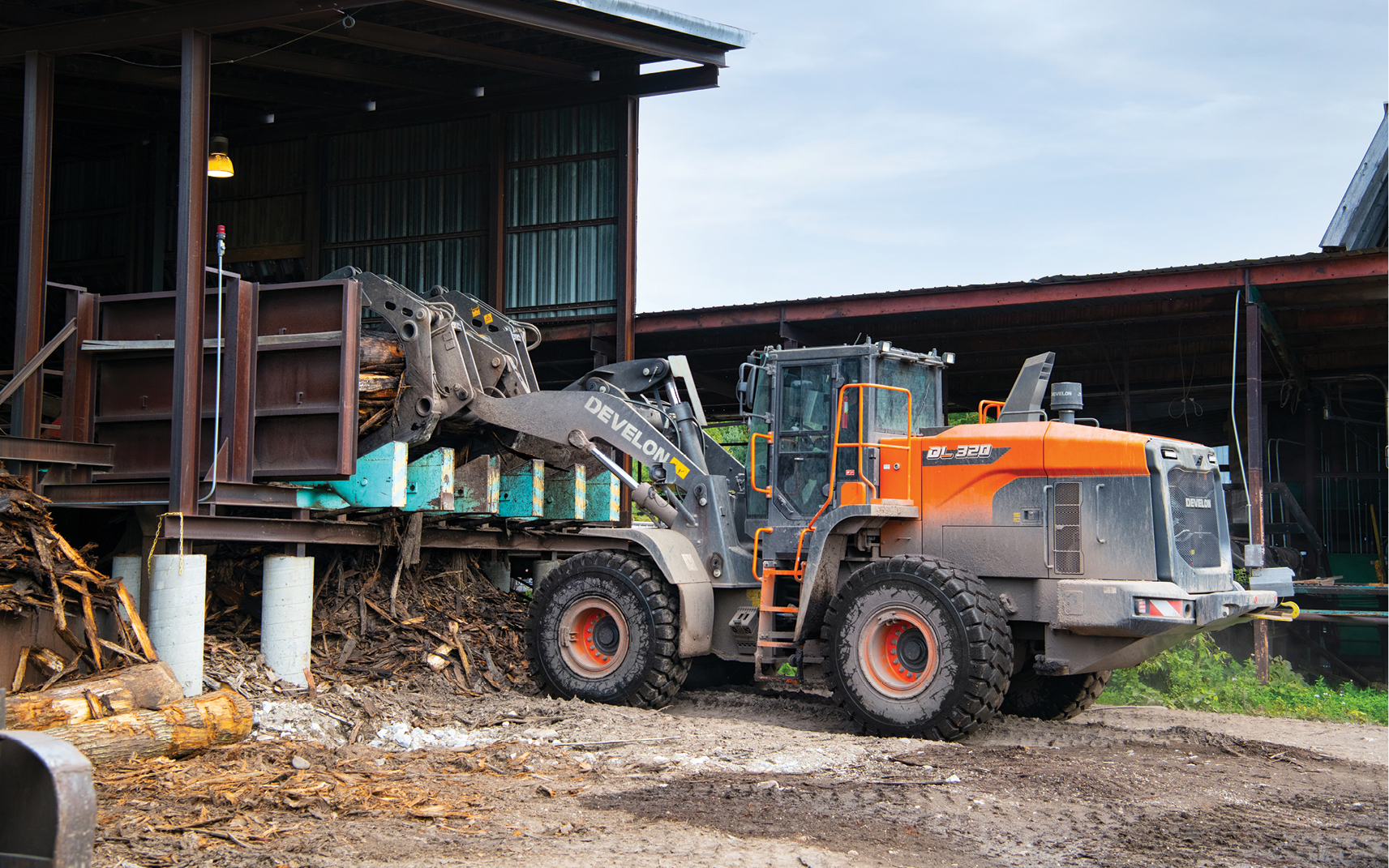 A DEVELON wheel loader operator unloads a stack of logs with a grapple attachment.